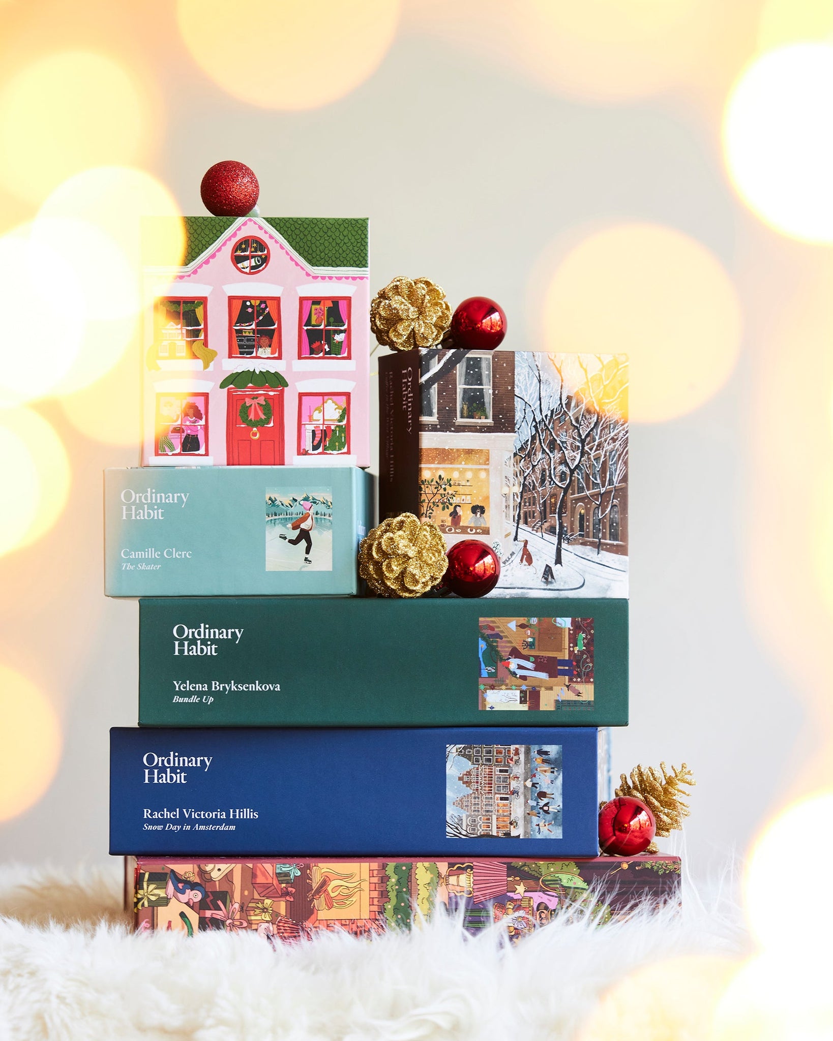 Stack of Ordinary Habit holiday themed puzzles with Christmas decorations on a blurred light background